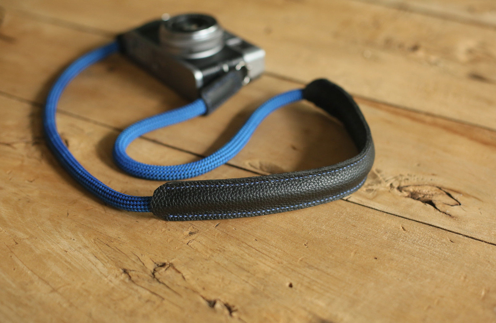 Blue climbing rope camera strap with leather shoulder pad on wooden table