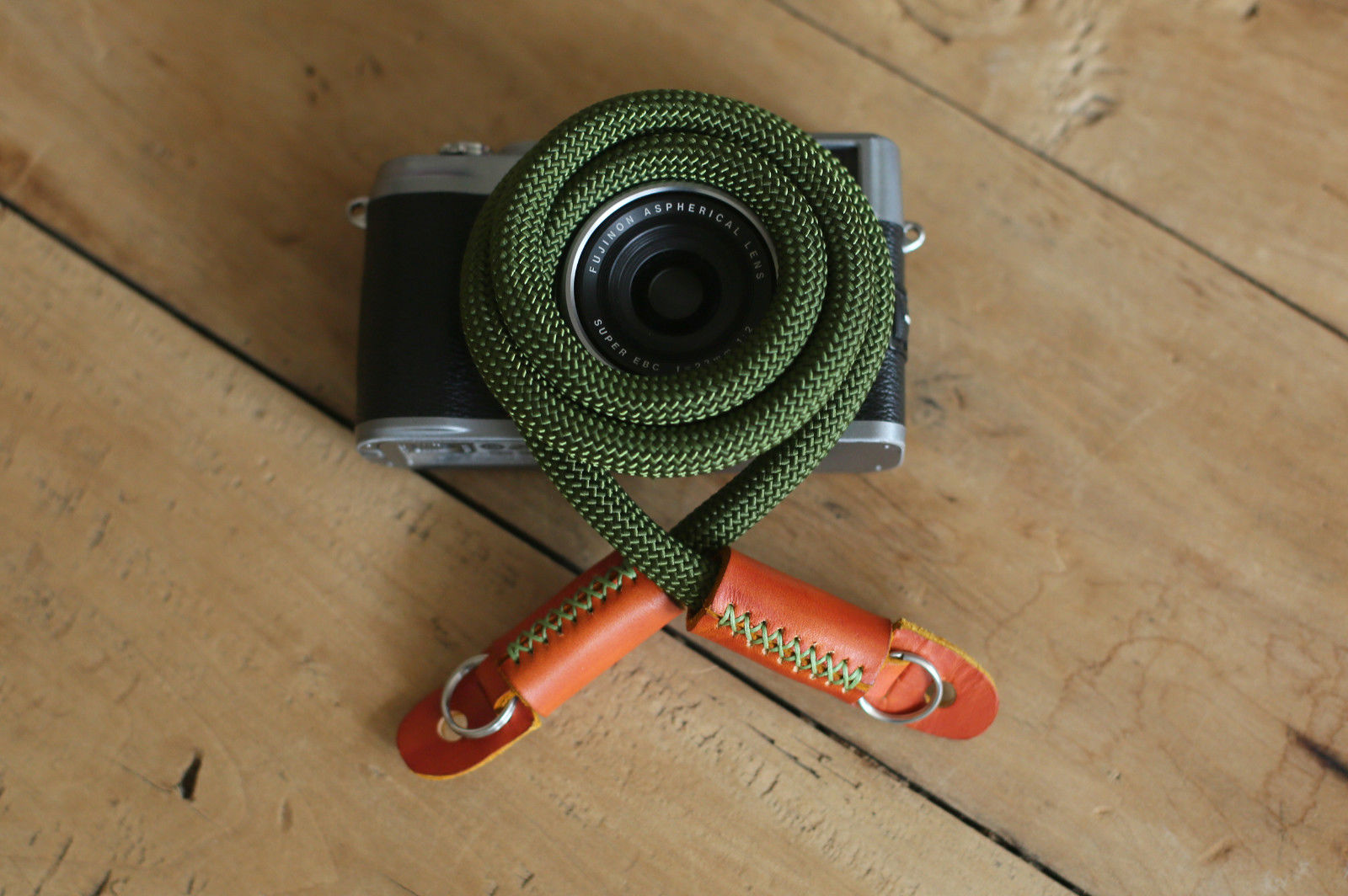 Army green camera strap with leather ends on wood surface