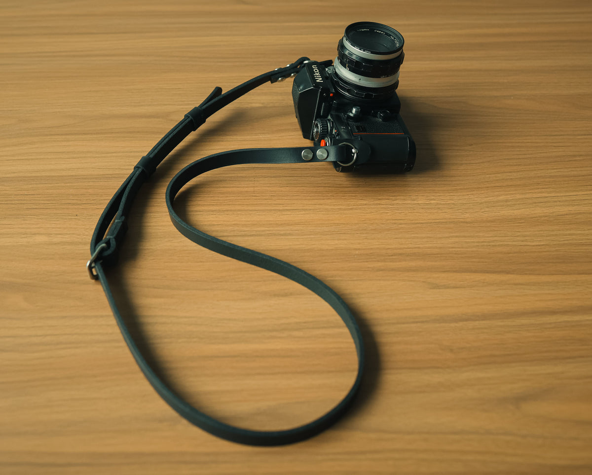 Adjustable black leather camera strap attached to a film camera