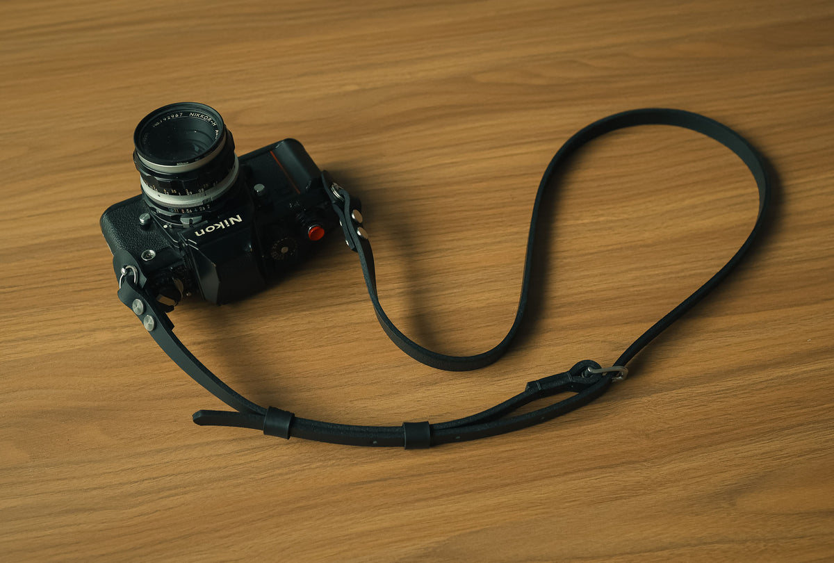 Full view of black leather camera strap beside a vintage camera