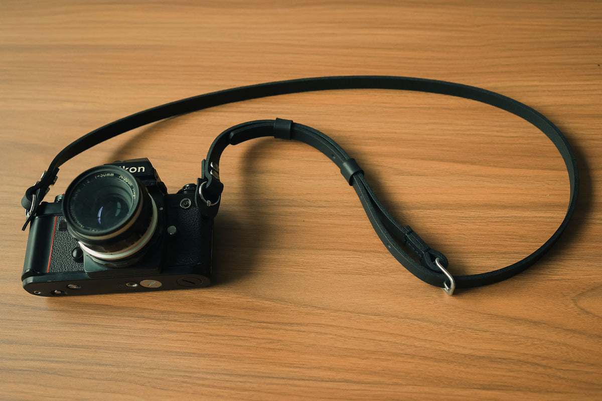 Black leather camera strap shown with a vintage film camera