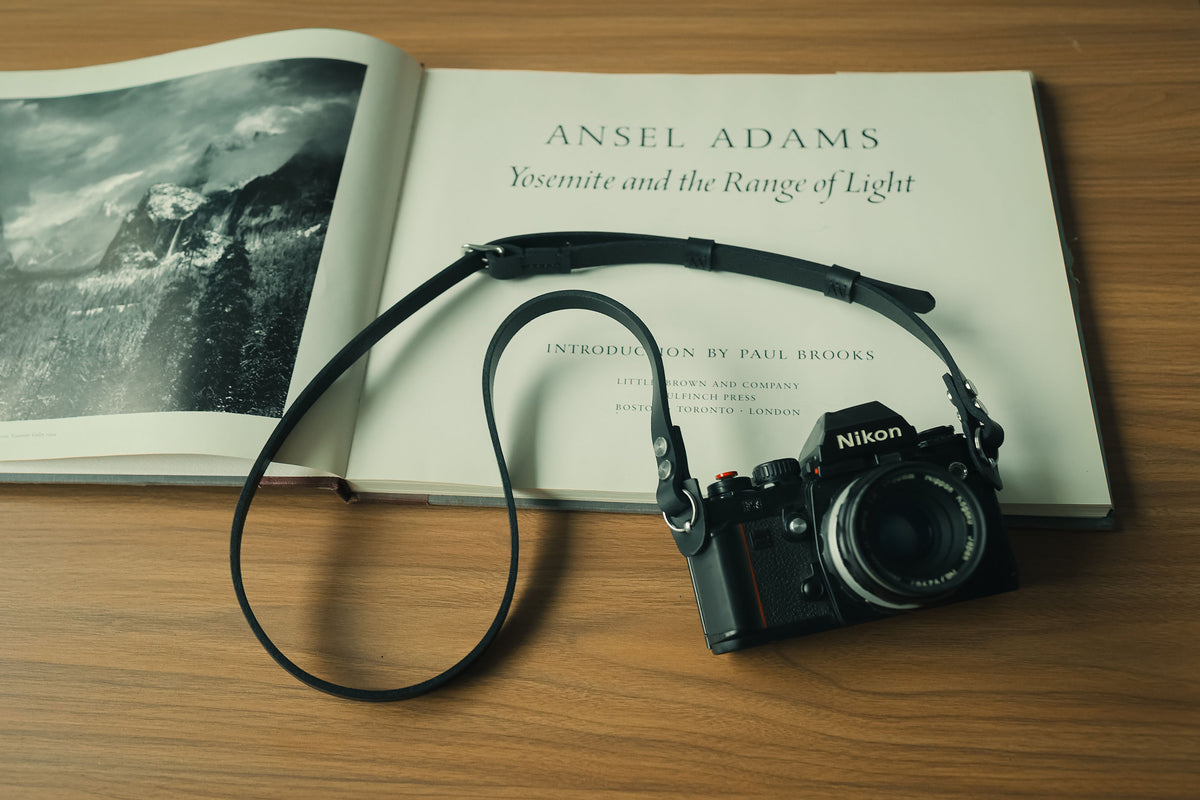 Black leather camera strap styled with a photography book
