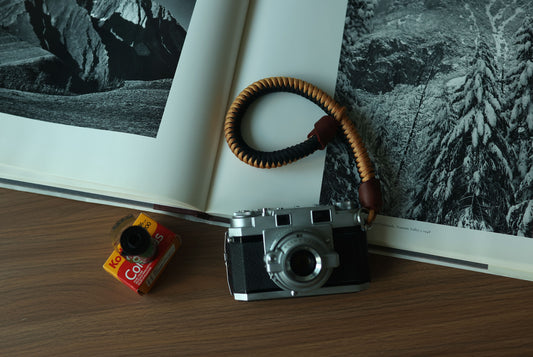 Top view of black and gold braided paracord camera wrist strap with brown leather ends