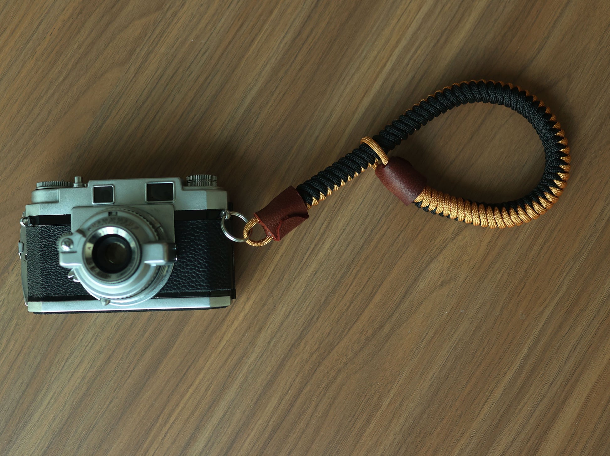 Flat lay of black and gold braided camera wrist strap with brown leather ends and vintage camera