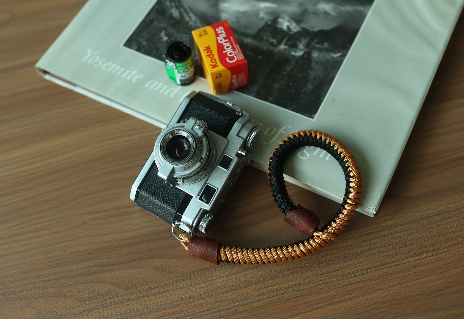 Black and gold braided paracord camera wrist strap with brown leather ends attached to a vintage camera