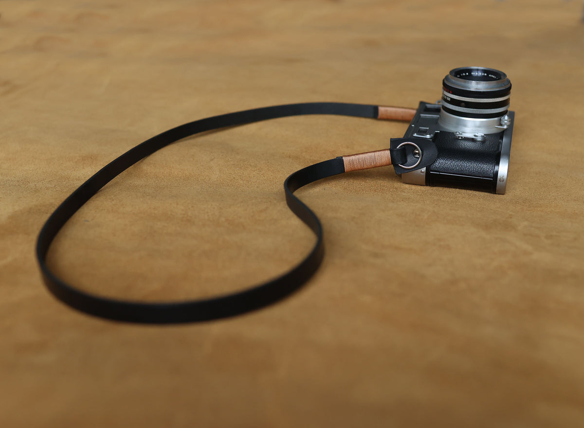 Black leather camera strap with tan waxed thread attached to a vintage camera