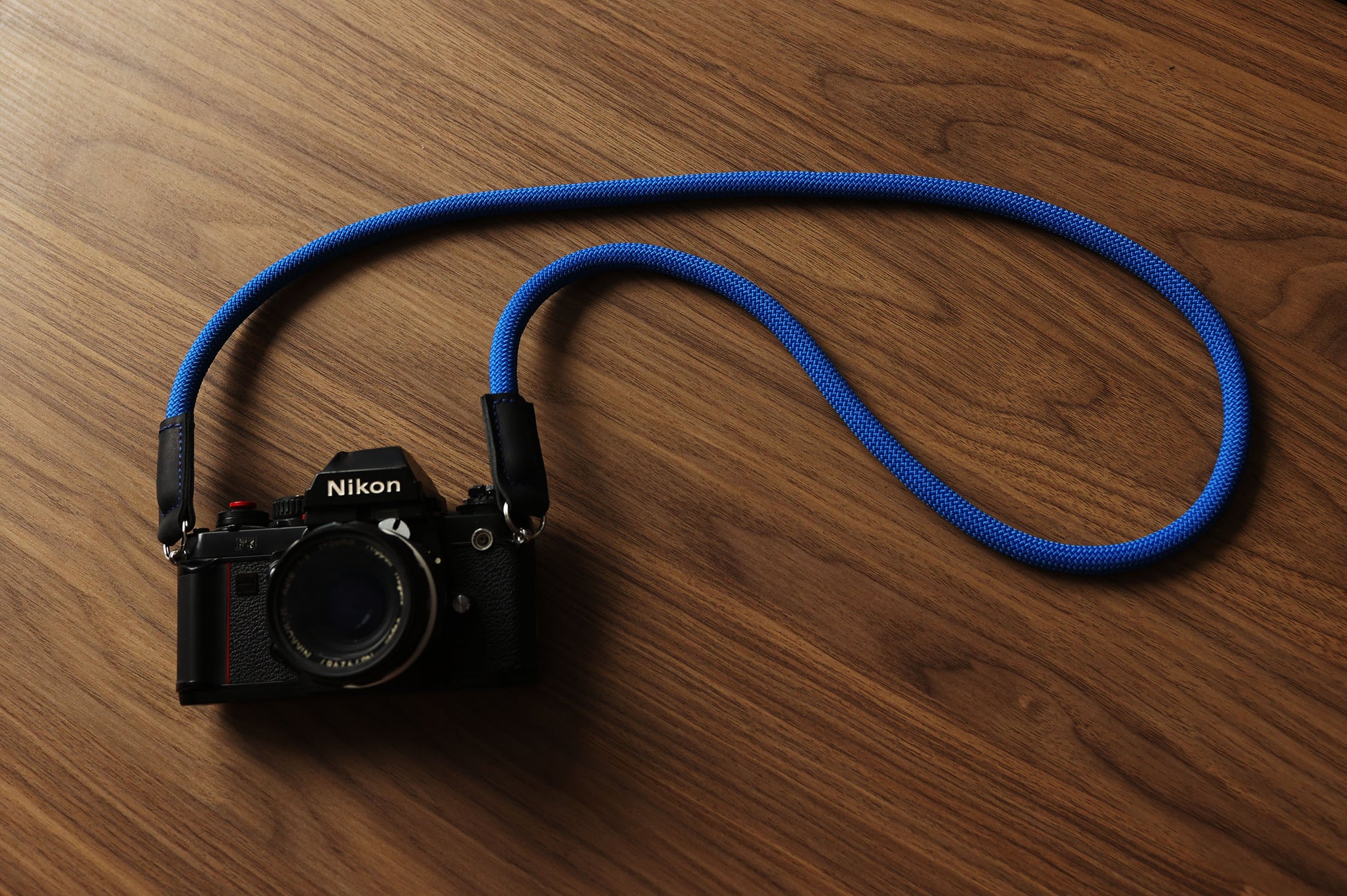 Blue camera strap photographed on walnut wood surface