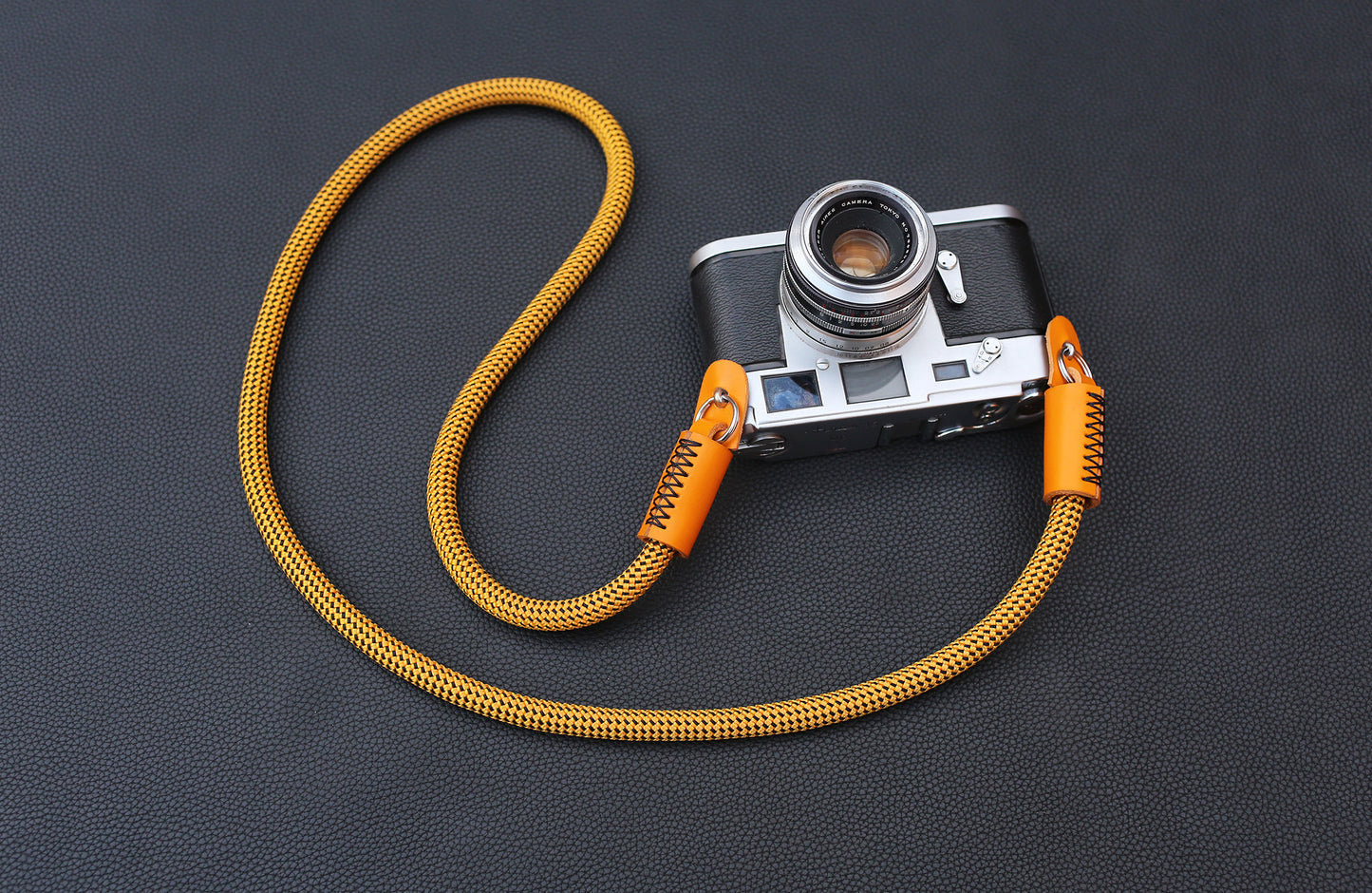 Close-up of gold rope camera strap with grained orange leather wrap