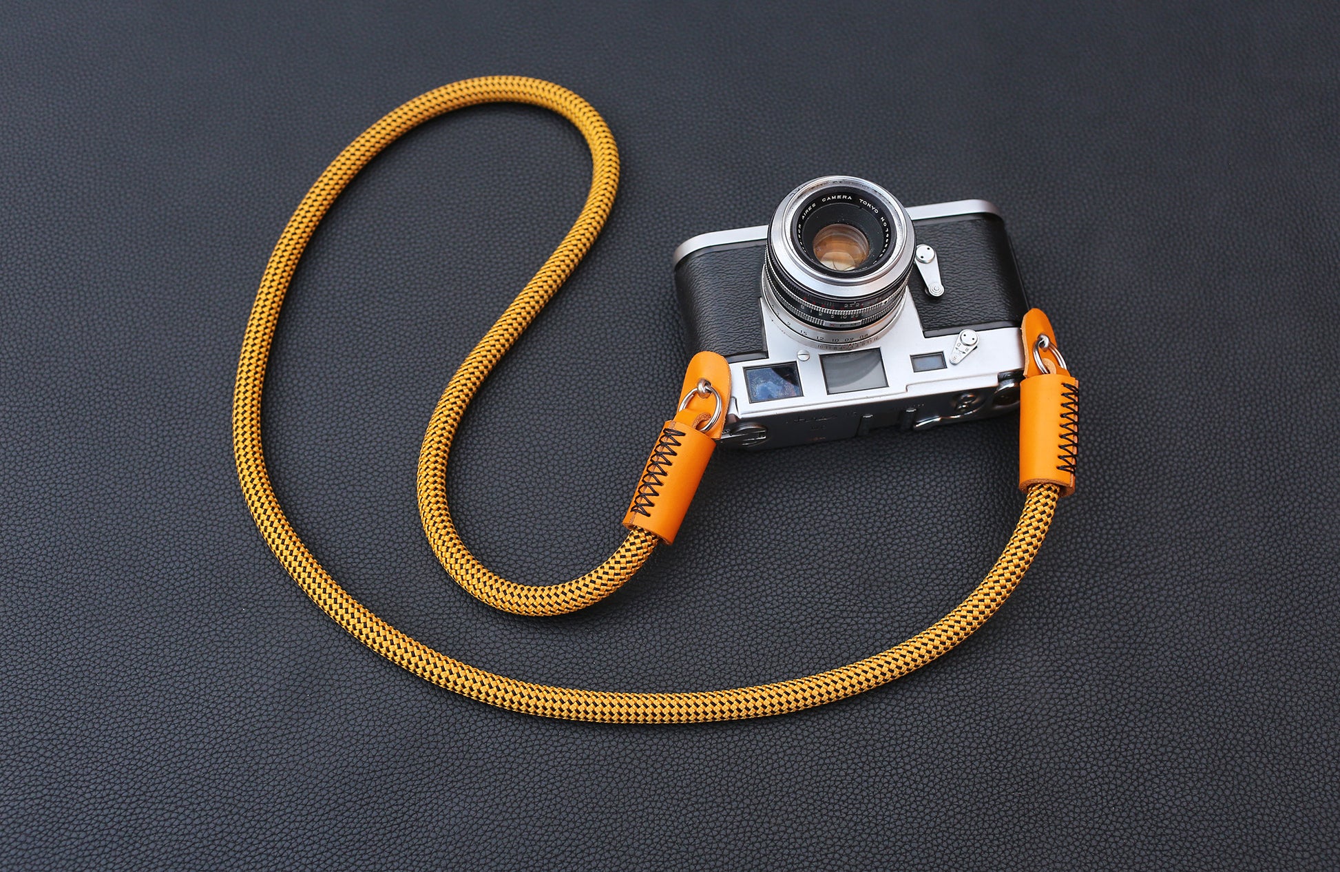 Close-up of gold rope camera strap with grained orange leather wrap