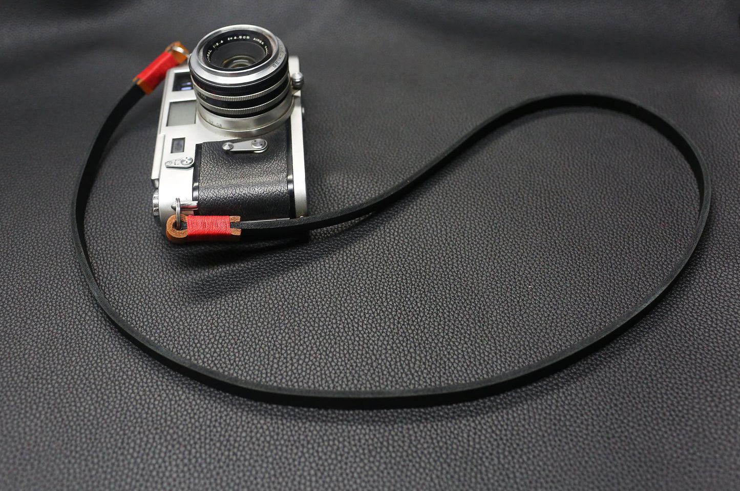 Black leather camera strap crafted by Windmup on textured black background.