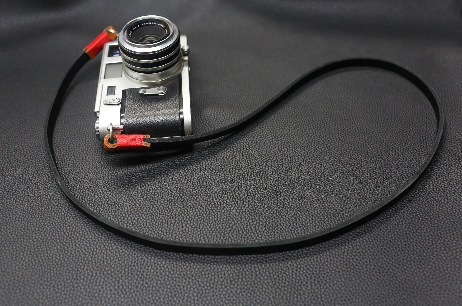 Black leather camera strap crafted by Windmup on textured black background.