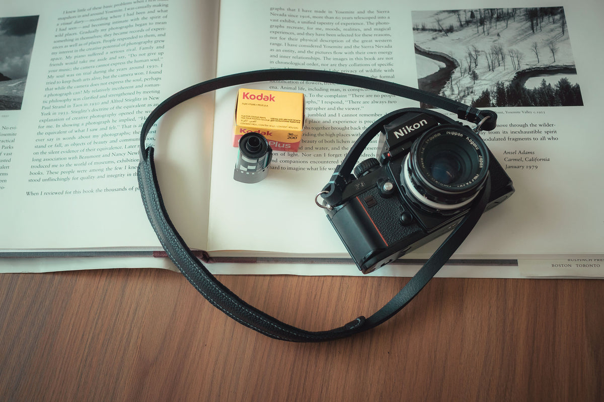 Handmade black leather camera strap with a wide shoulder pad and grey stitching