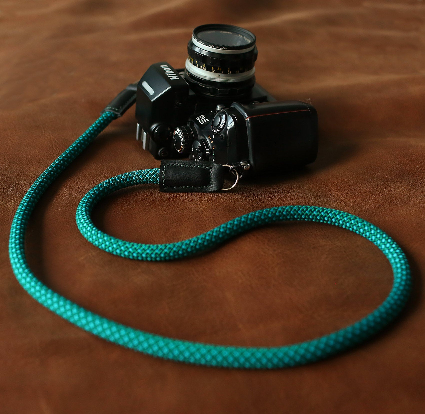Green rope camera strap coiled on brown leather background – 105cm length