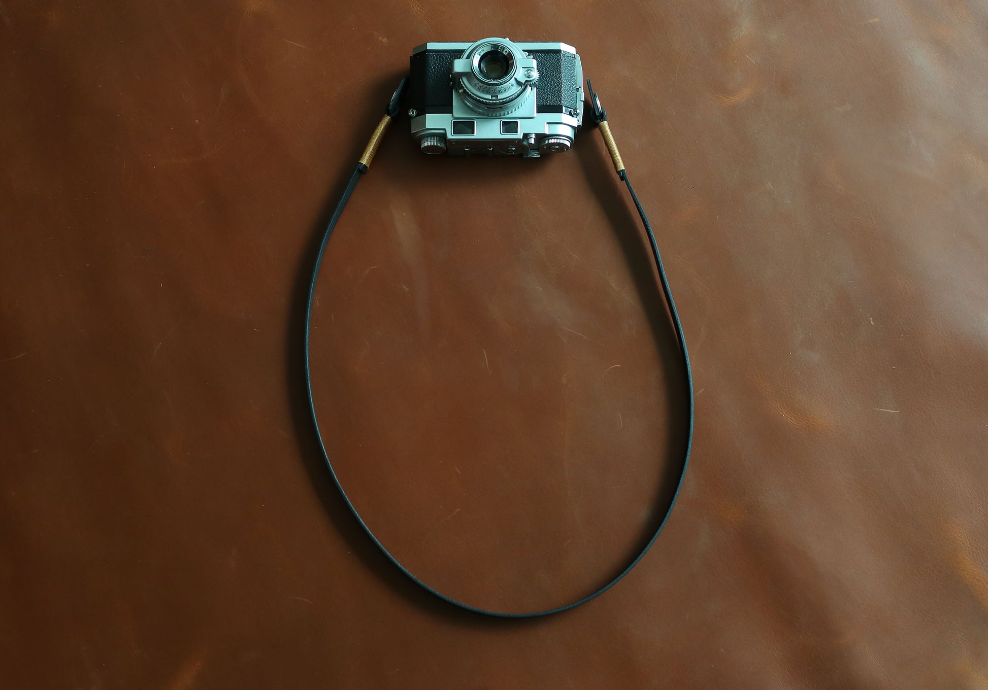 Minimalist 10mm wide black leather camera strap with durable tan wax thread stitching