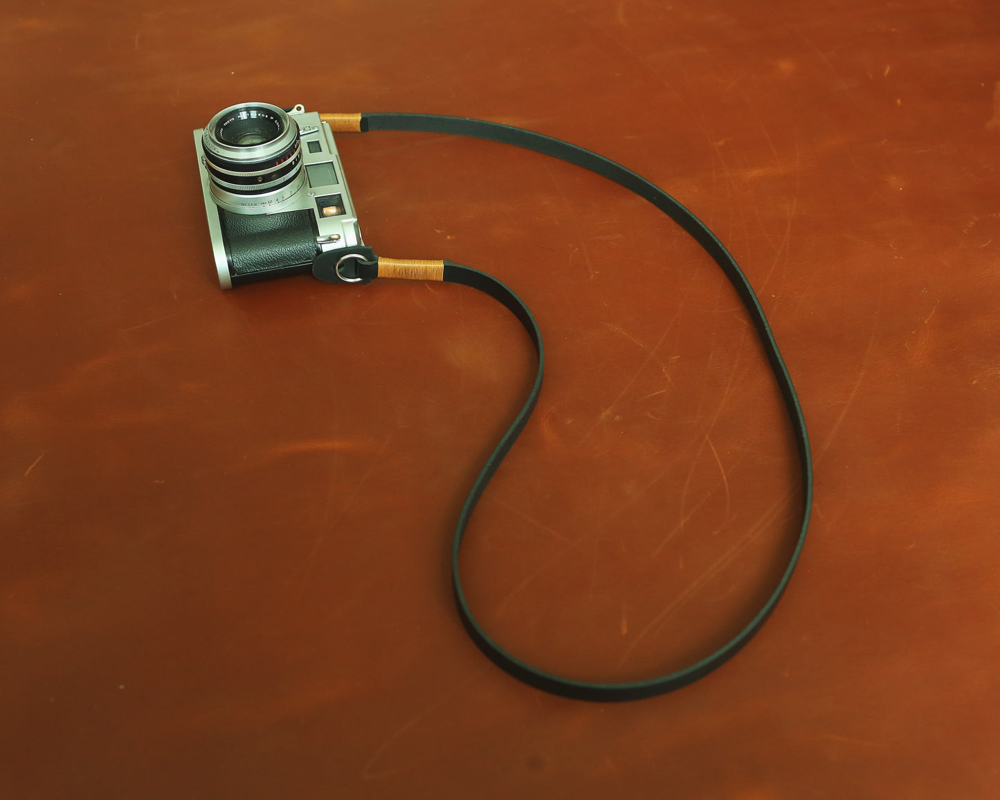 Minimalist black camera neck strap featuring distinctive tan wax thread hand-stitching.