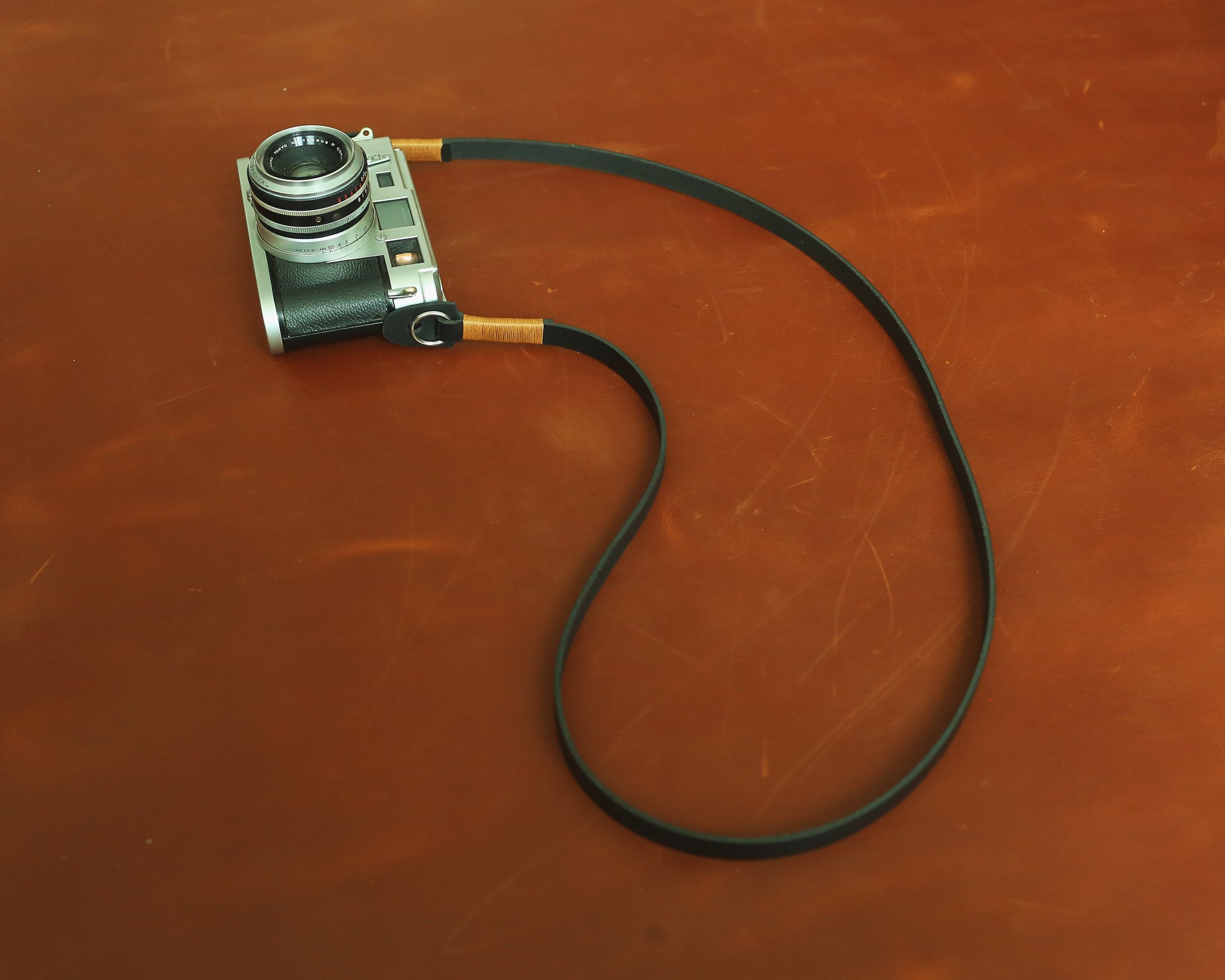 Minimalist black camera neck strap featuring distinctive tan wax thread hand-stitching.