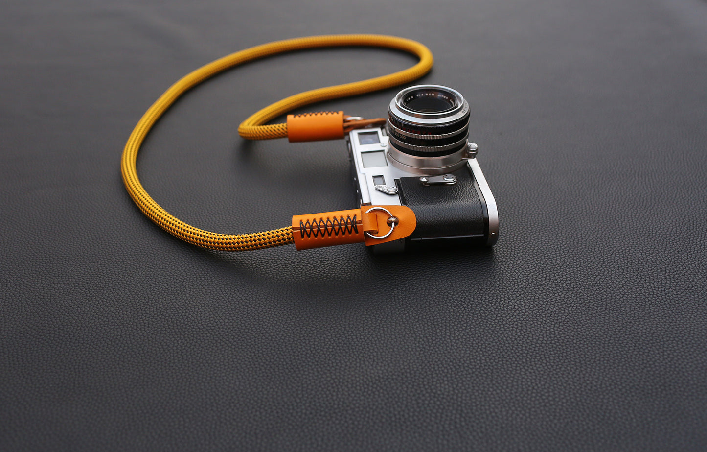 Orange leather connection detail on gold rope camera strap