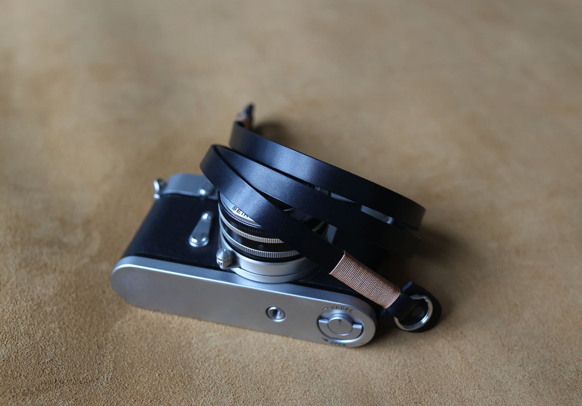 Soft black leather camera strap with subtle tan waxed thread shown in a flat lay
