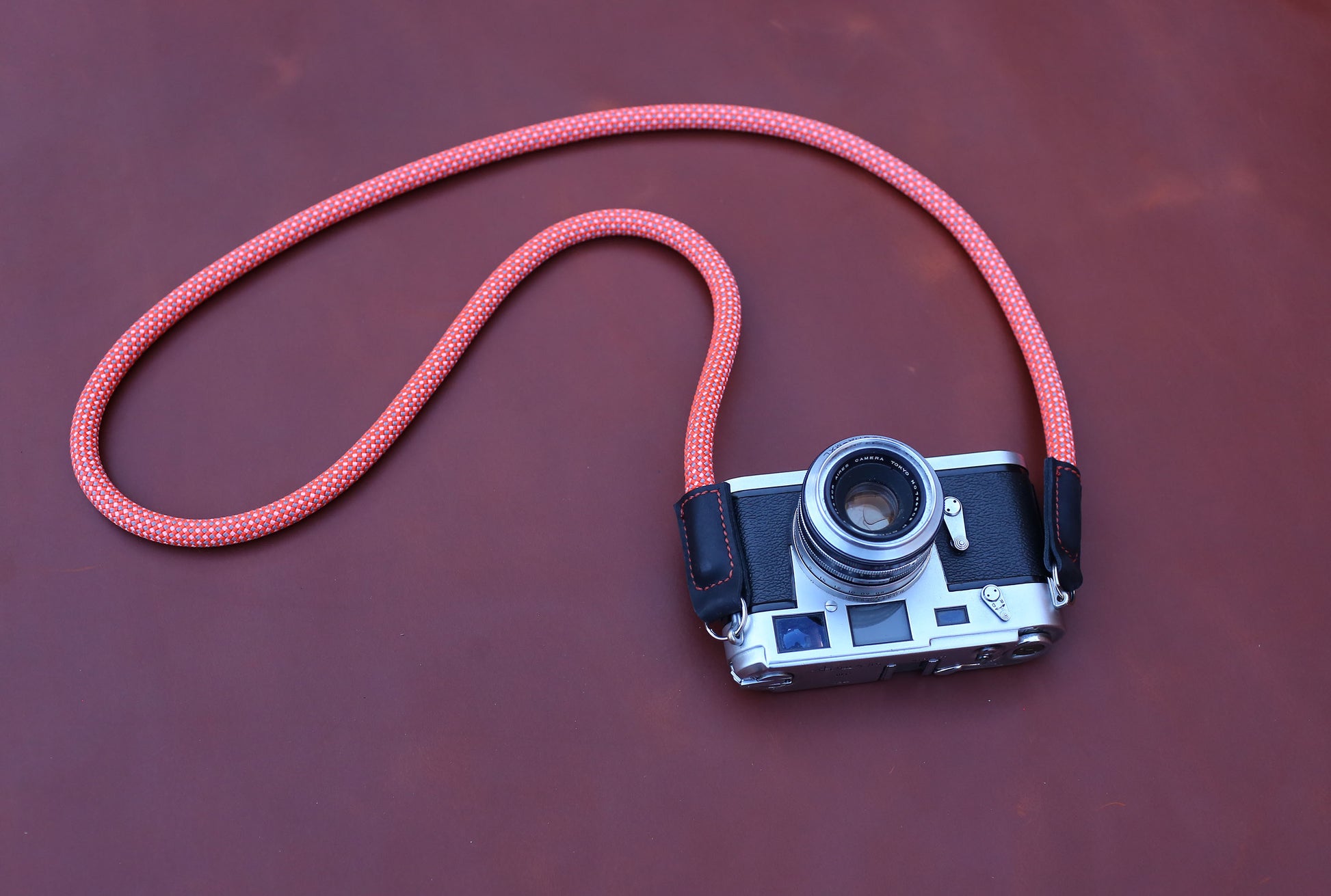 Flatlay of Spotted Crimson camera strap on premium brown leather background.