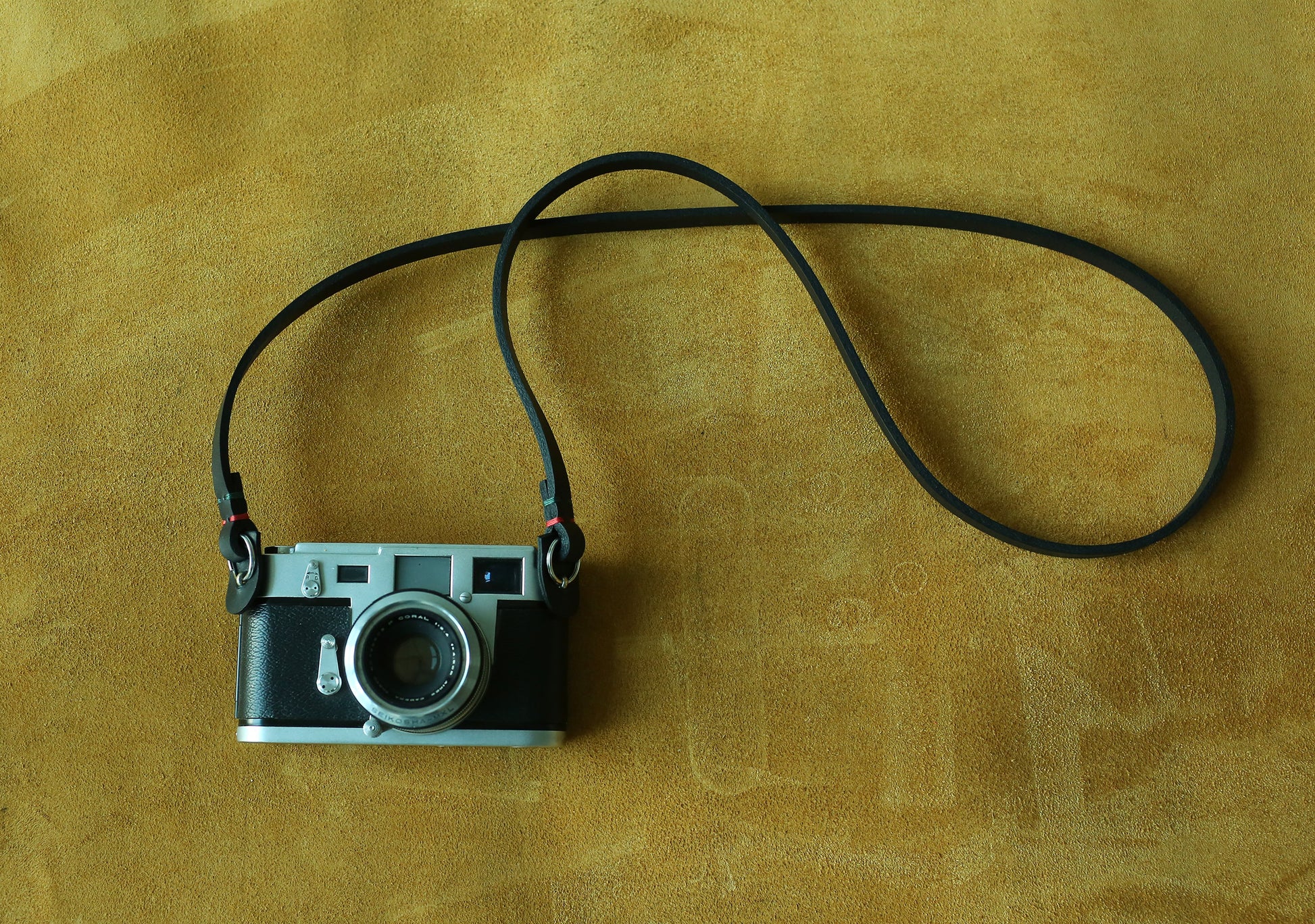 A Windmup stealth black leather camera strap featuring unique red and green hand-stitching