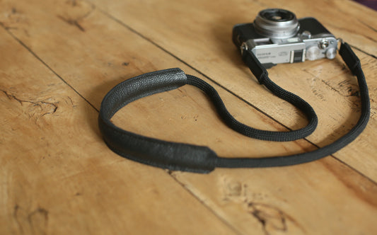 Black climbing rope camera strap with leather shoulder pad placed on wooden table