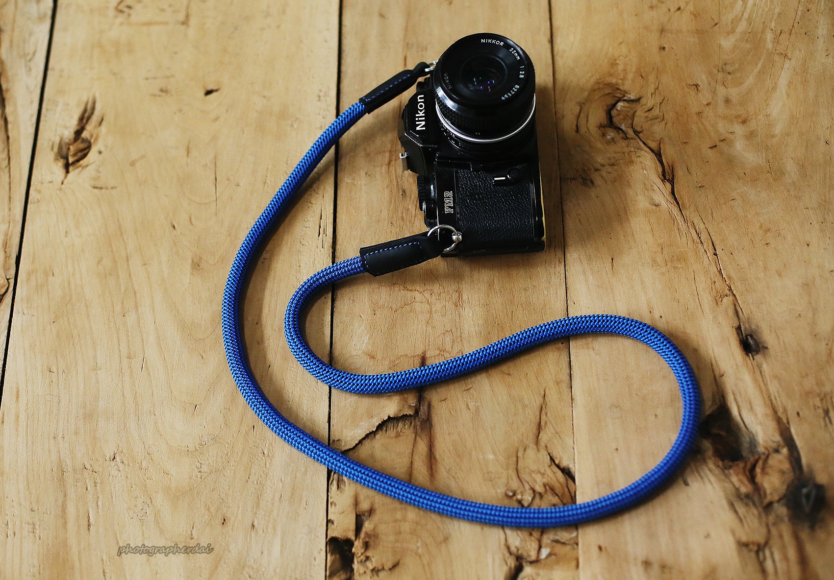 Blue 10mm rope camera strap with black dotted weave and leather ends on wooden table