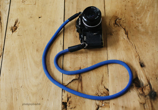 Blue 10mm rope camera strap with black dotted weave and leather ends on wooden table