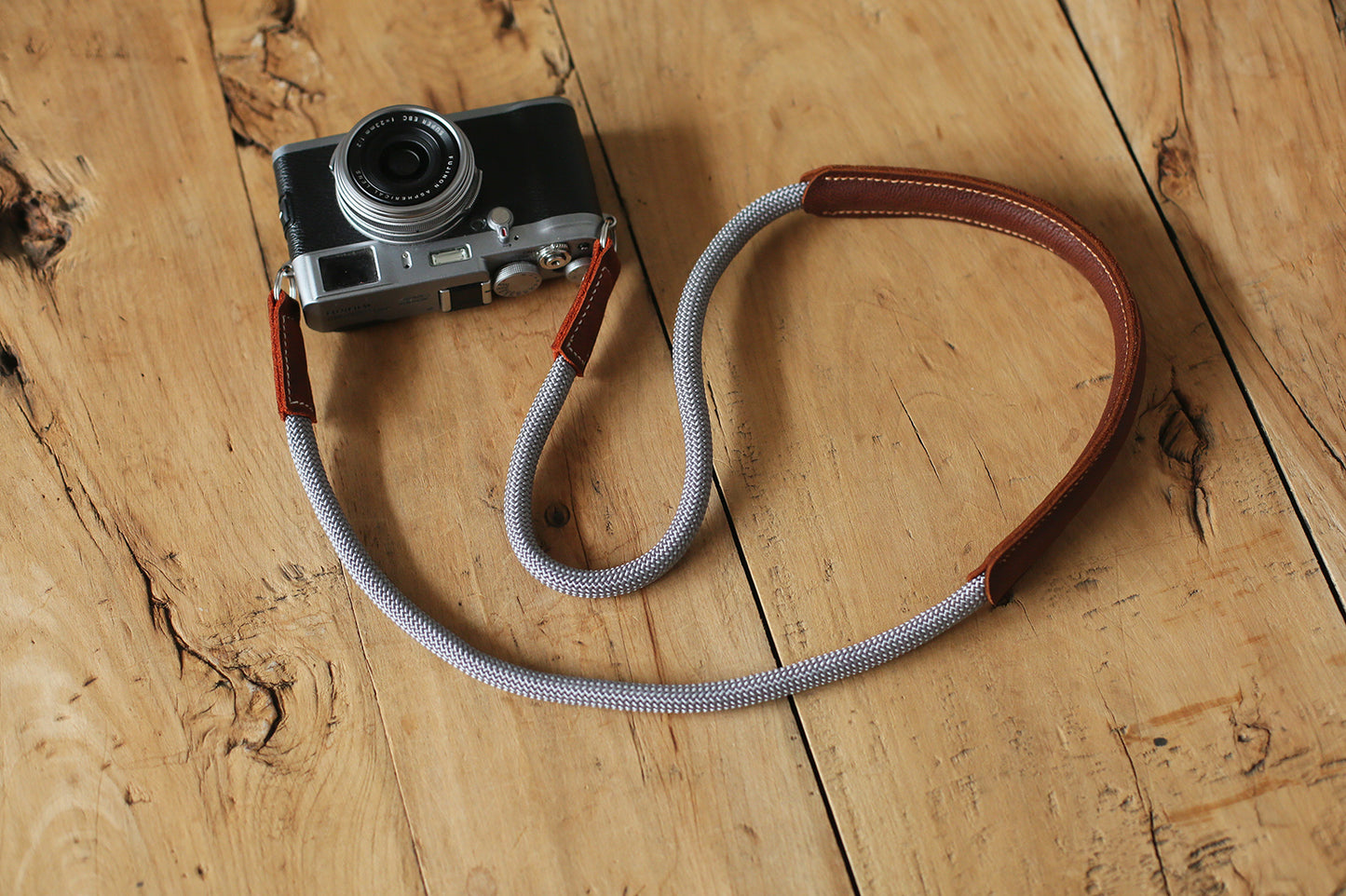Gray rope camera strap with brown leather pad on wooden surface