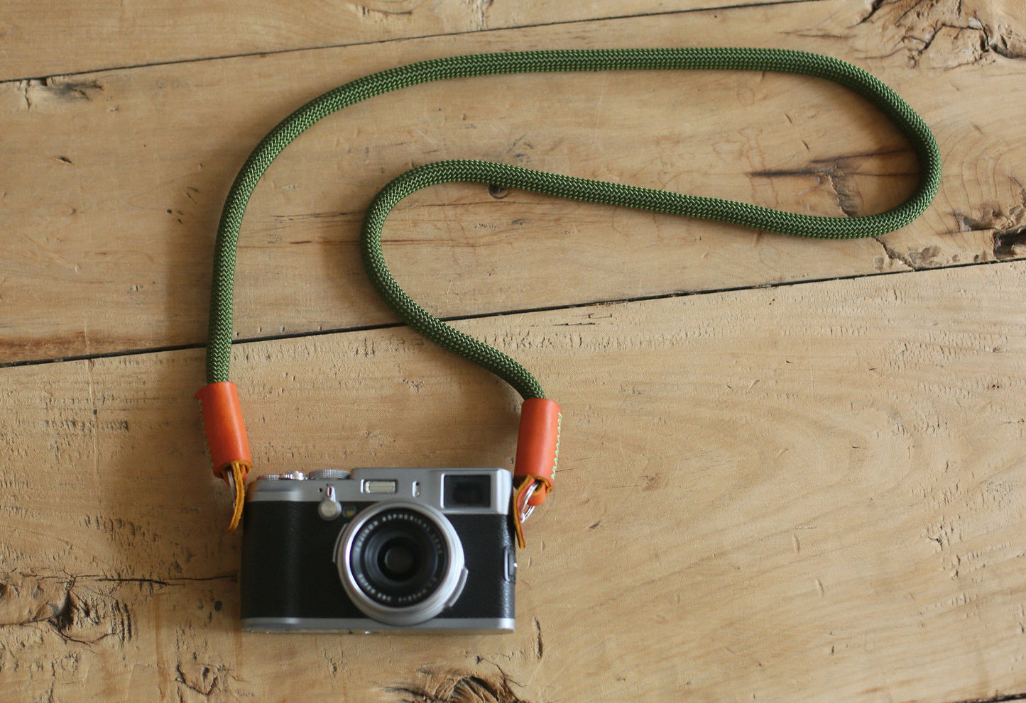 Army green camera strap with leather ends on wood surface