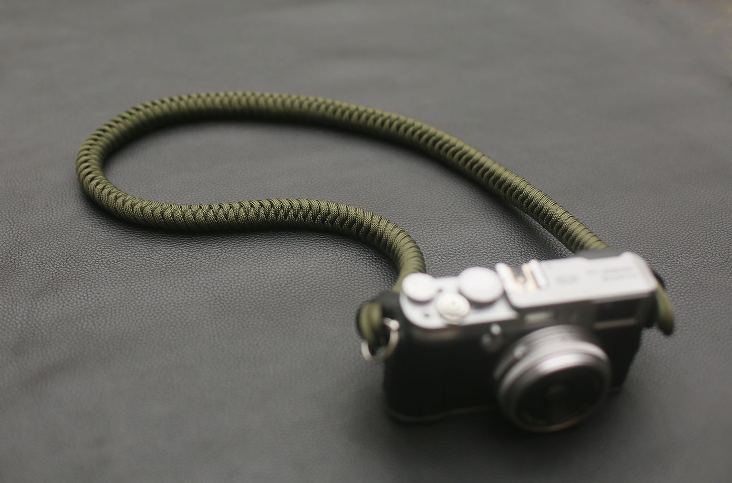 Military-inspired olive camera strap coiled on black leather surface
