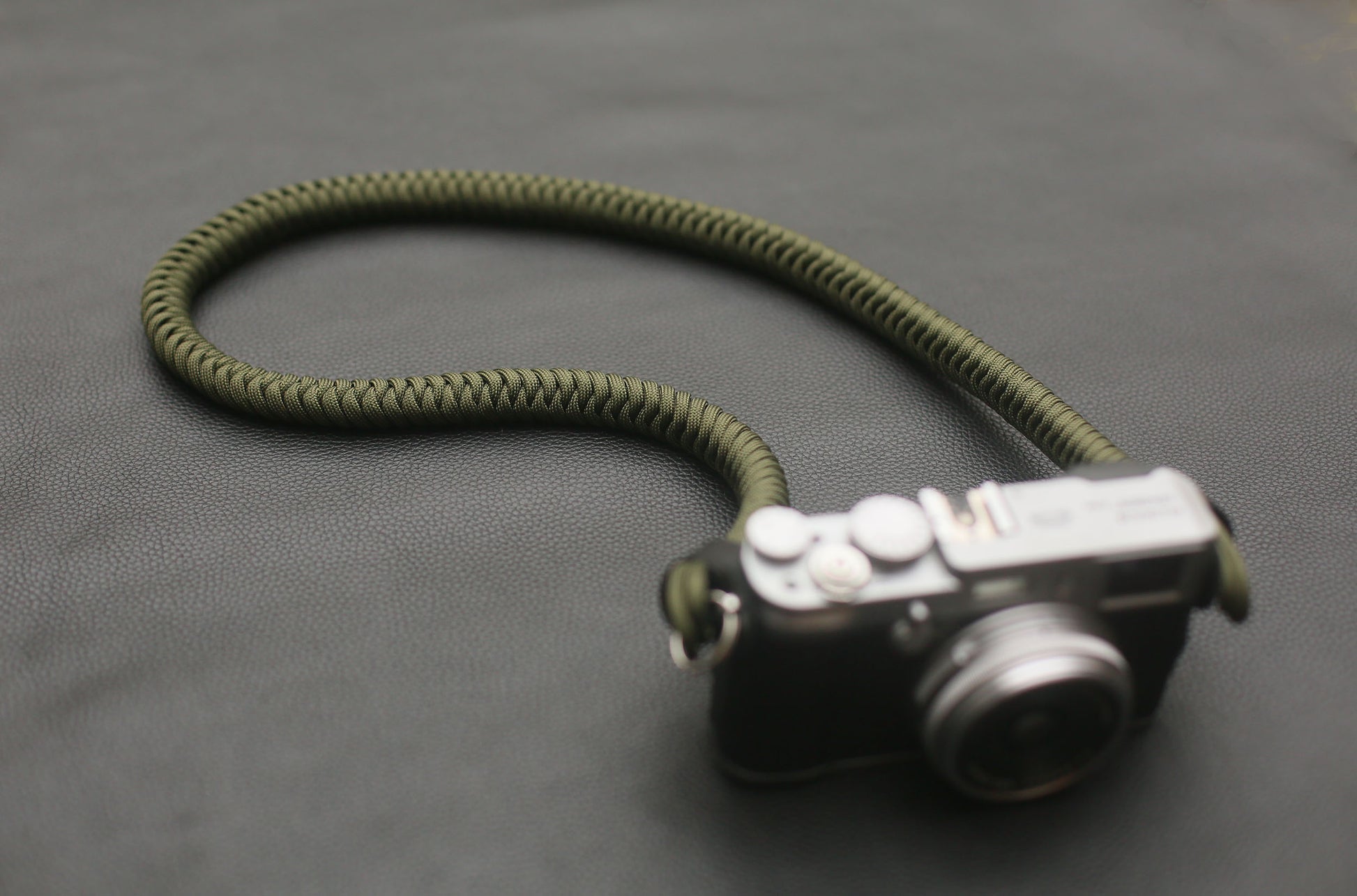 Military-inspired olive camera strap coiled on black leather surface