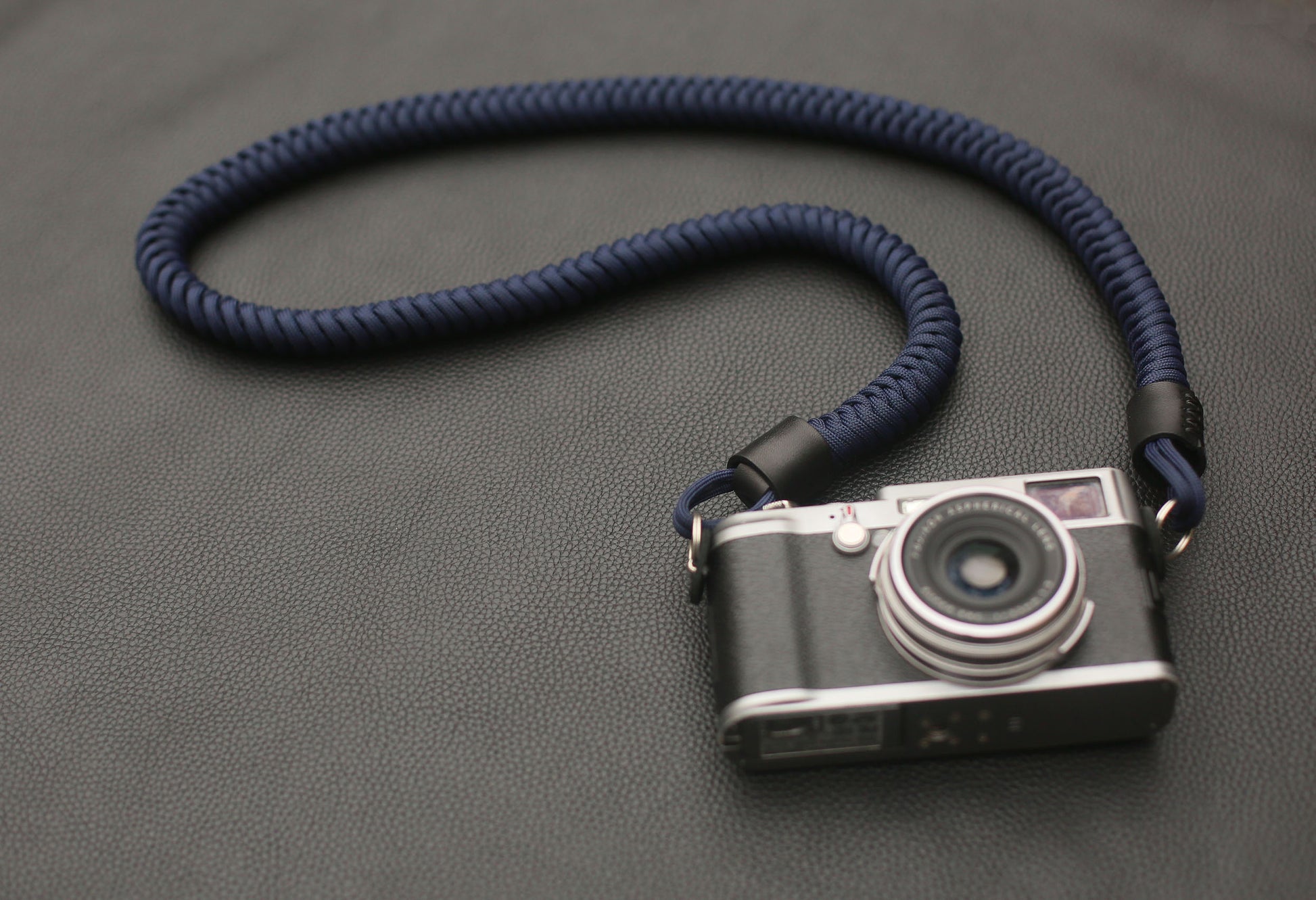 Navy blue paracord camera strap coiled on leather background