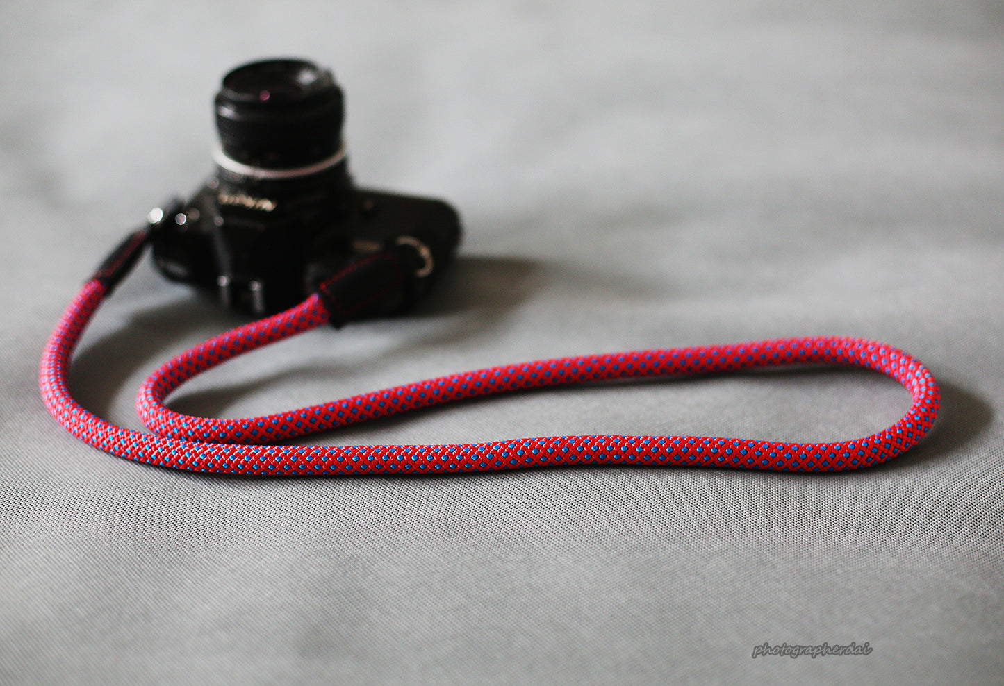 Purple camera strap resting on wooden table beside compact camera