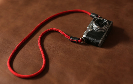 Red 8mm rope camera strap with leather ends laid on brown leather surface