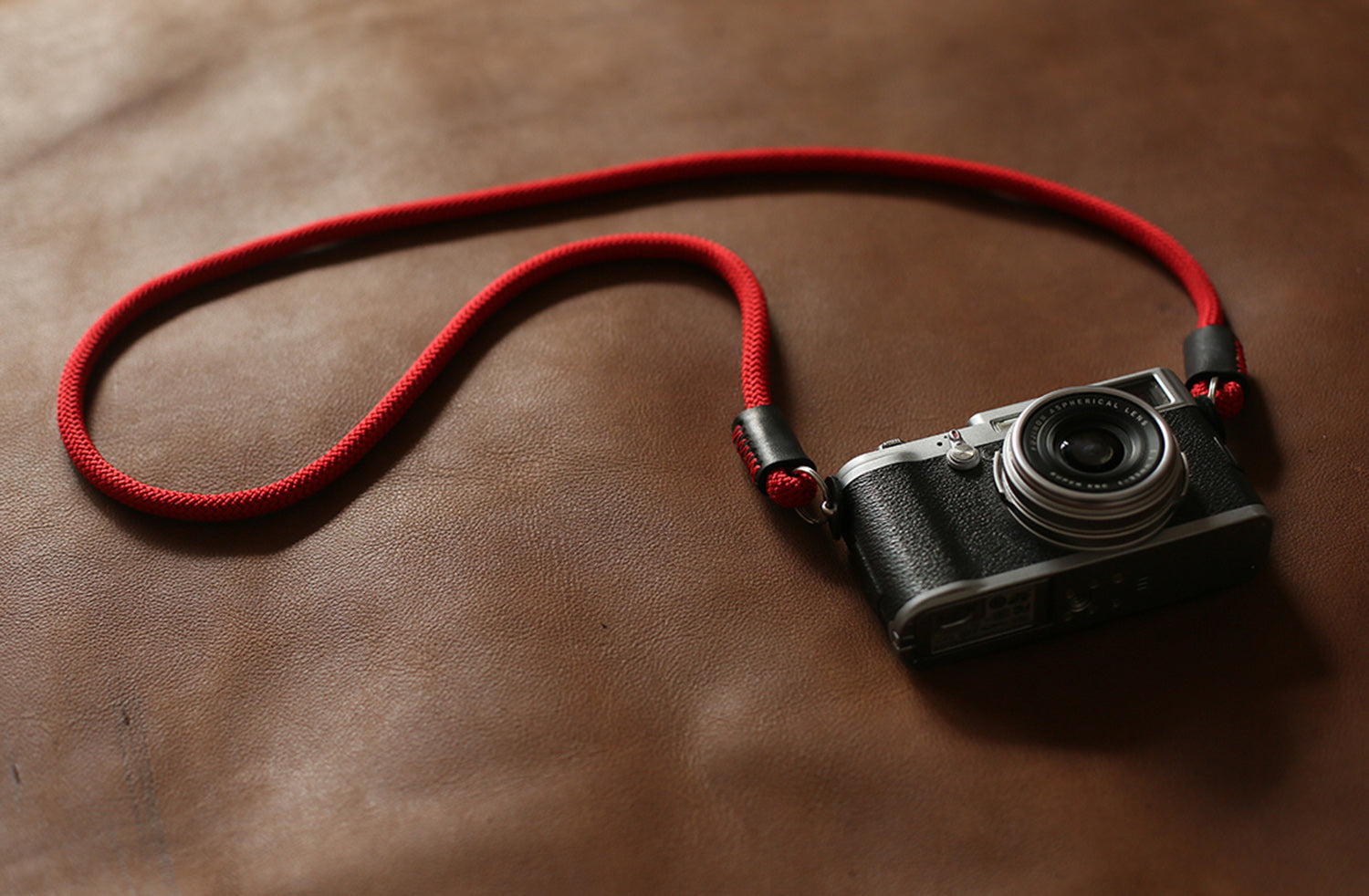 Red rope strap attached to compact film camera on leather background