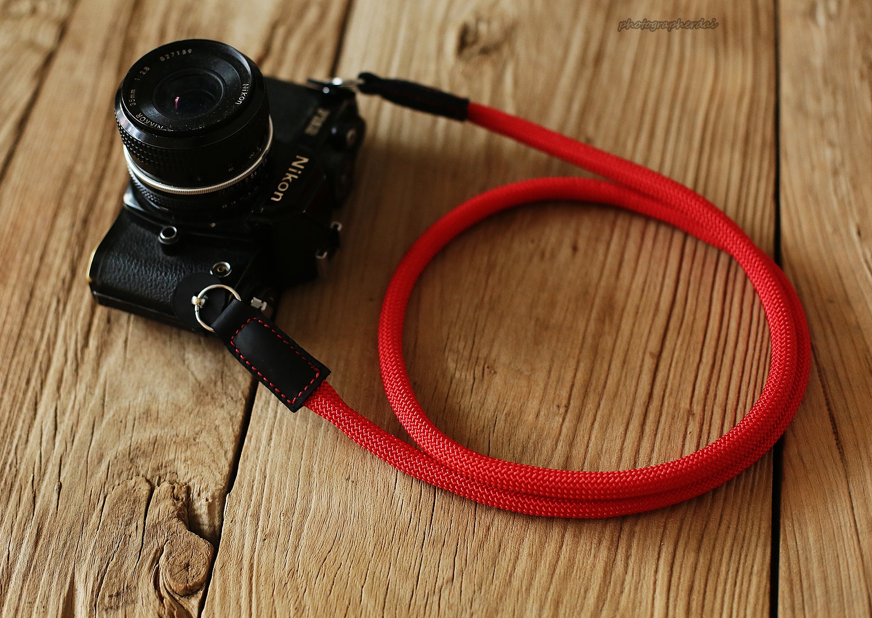 Flat lay of red rope camera strap with leather ends on wooden background