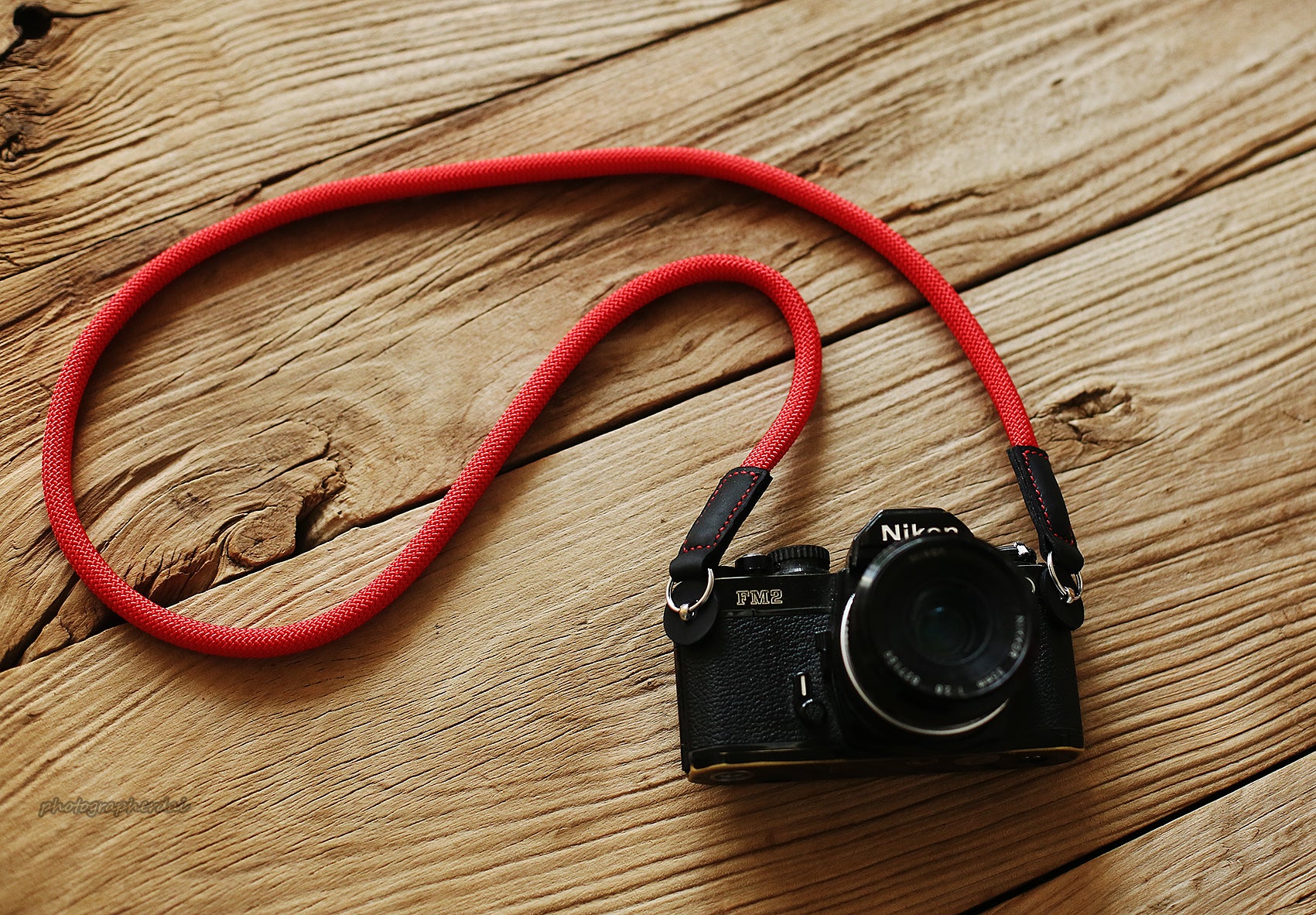 Full length view of red rope camera strap laid out on wood surface