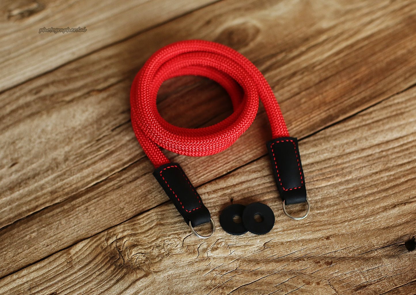 Minimal product scene of red rope camera strap beside camera on table