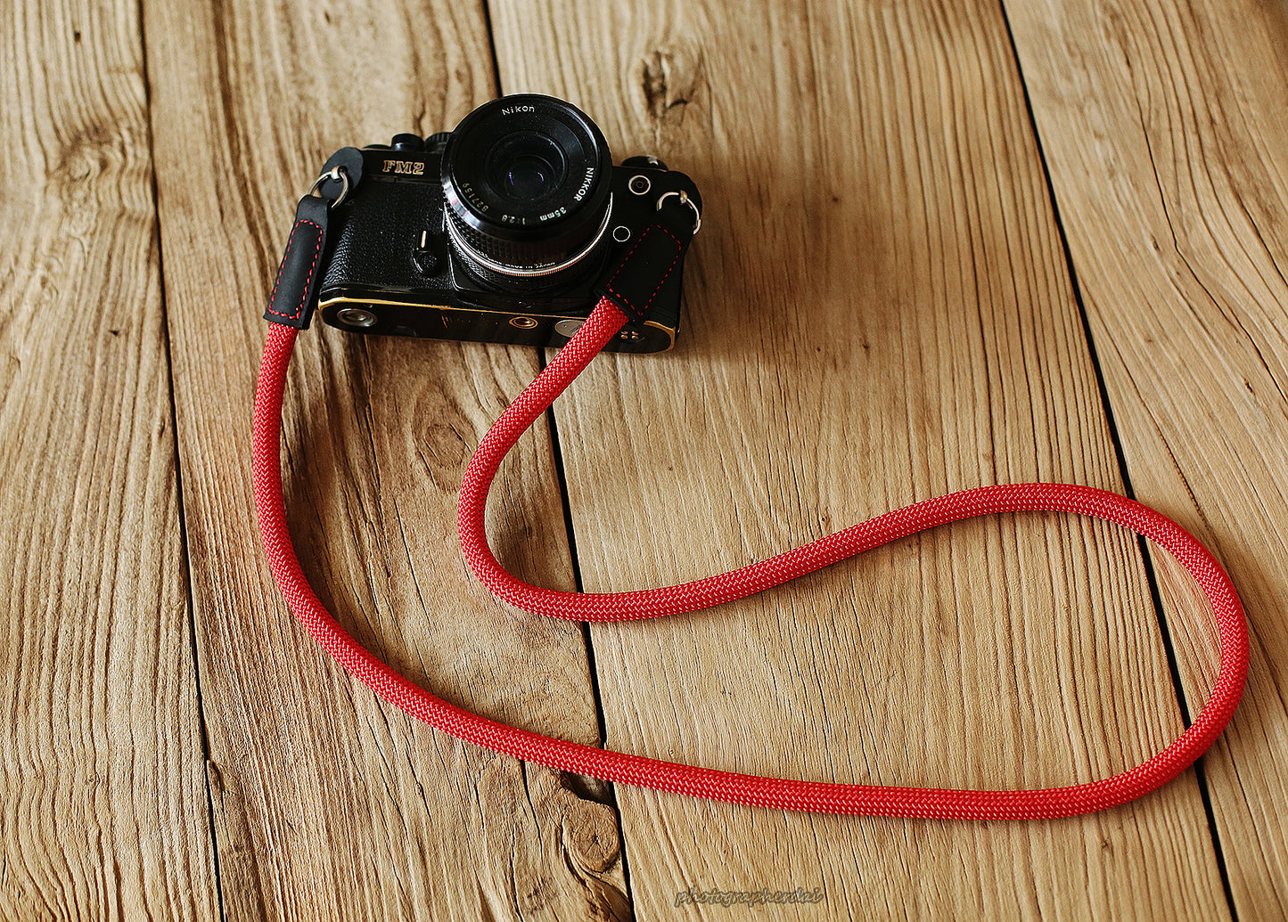 Bright red 10mm rope camera strap with black leather ends on wooden table
