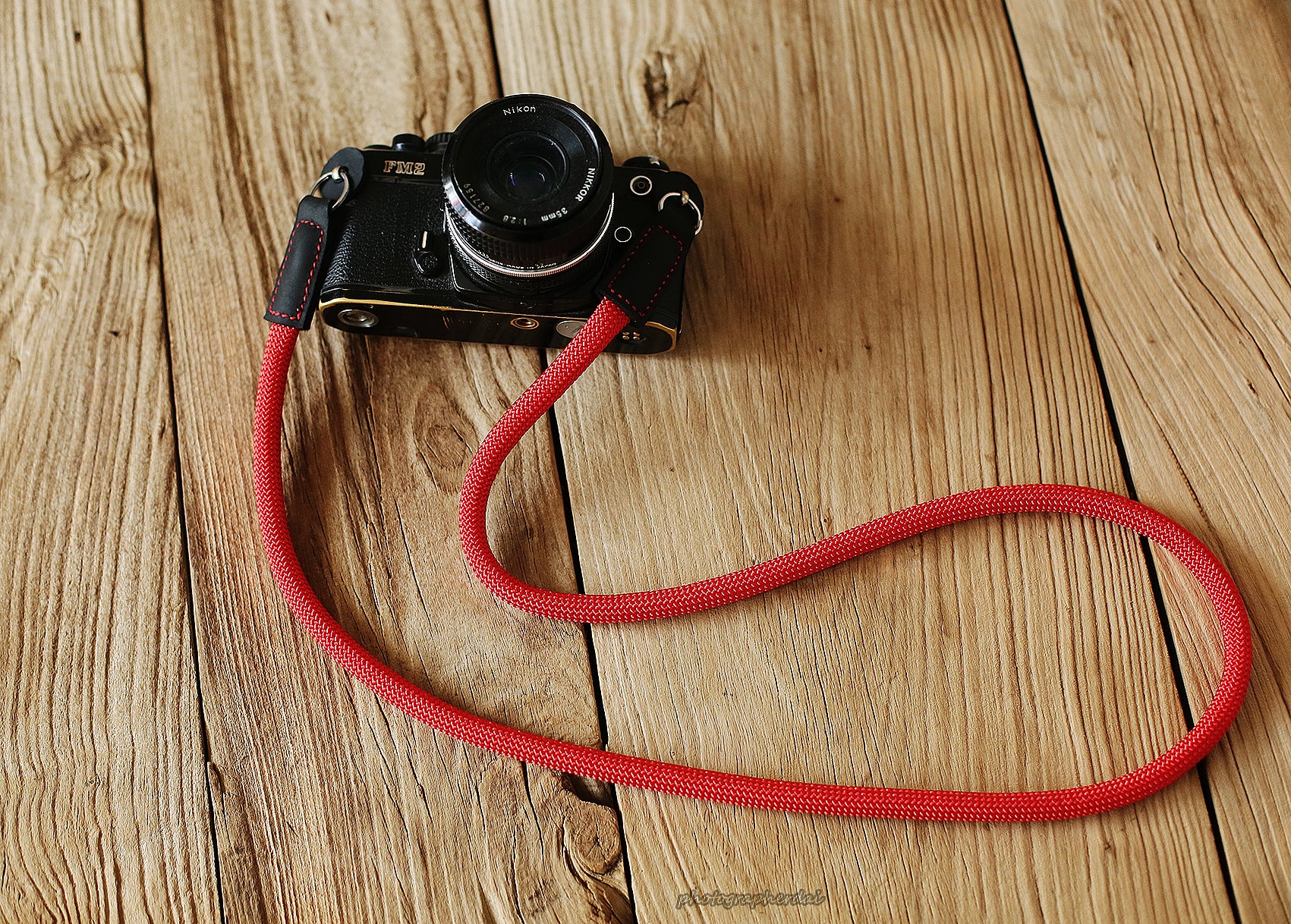 Bright red 10mm rope camera strap with black leather ends on wooden table
