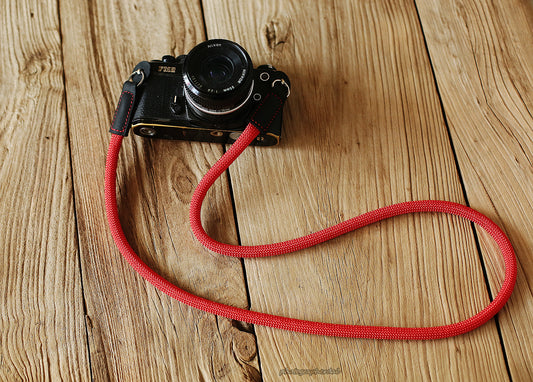 Bright red 10mm rope camera strap with black leather ends on wooden table
