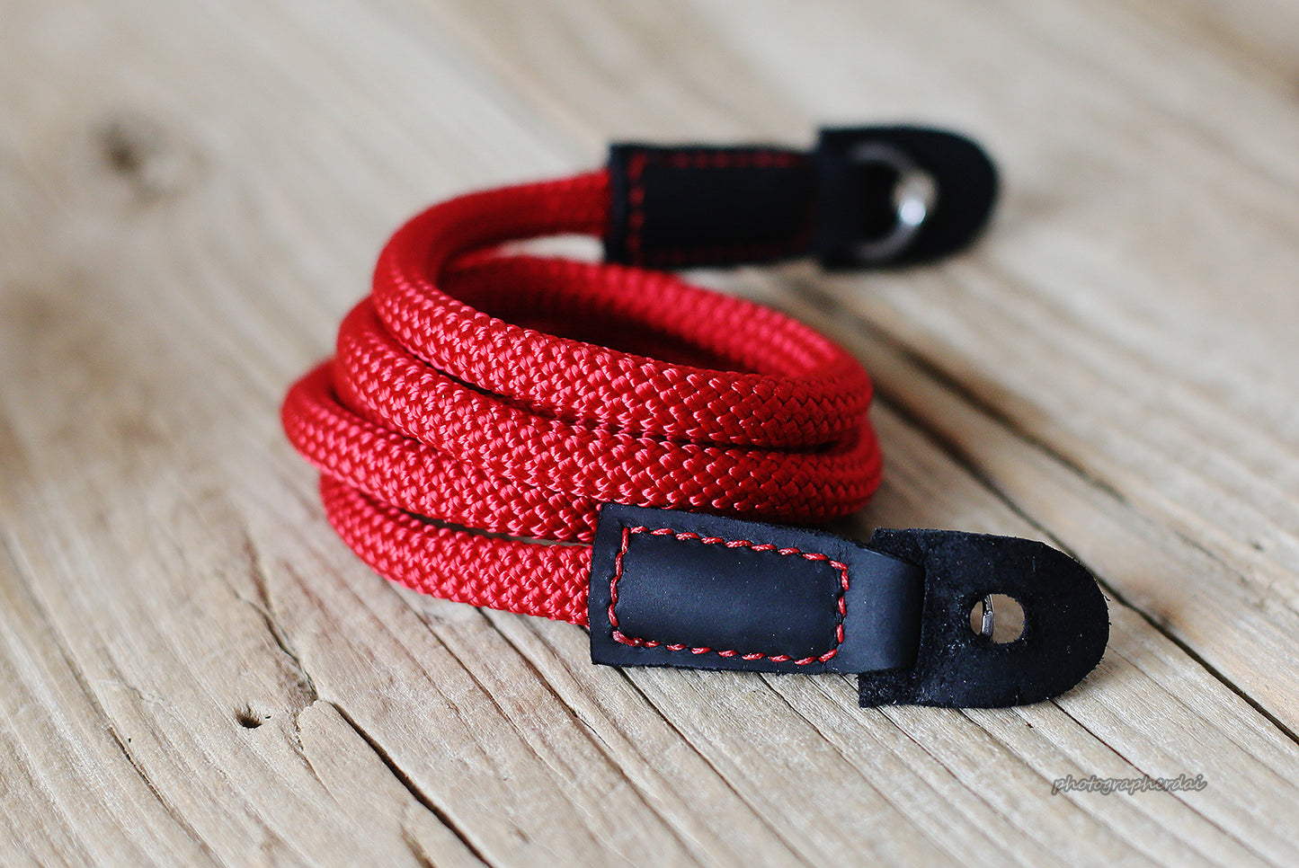 Red rope camera strap with black leather ends on wooden table