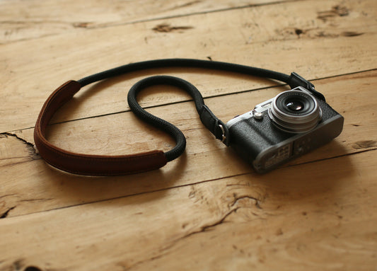 black rope camera strap with brown leather shoulder pad on wooden table